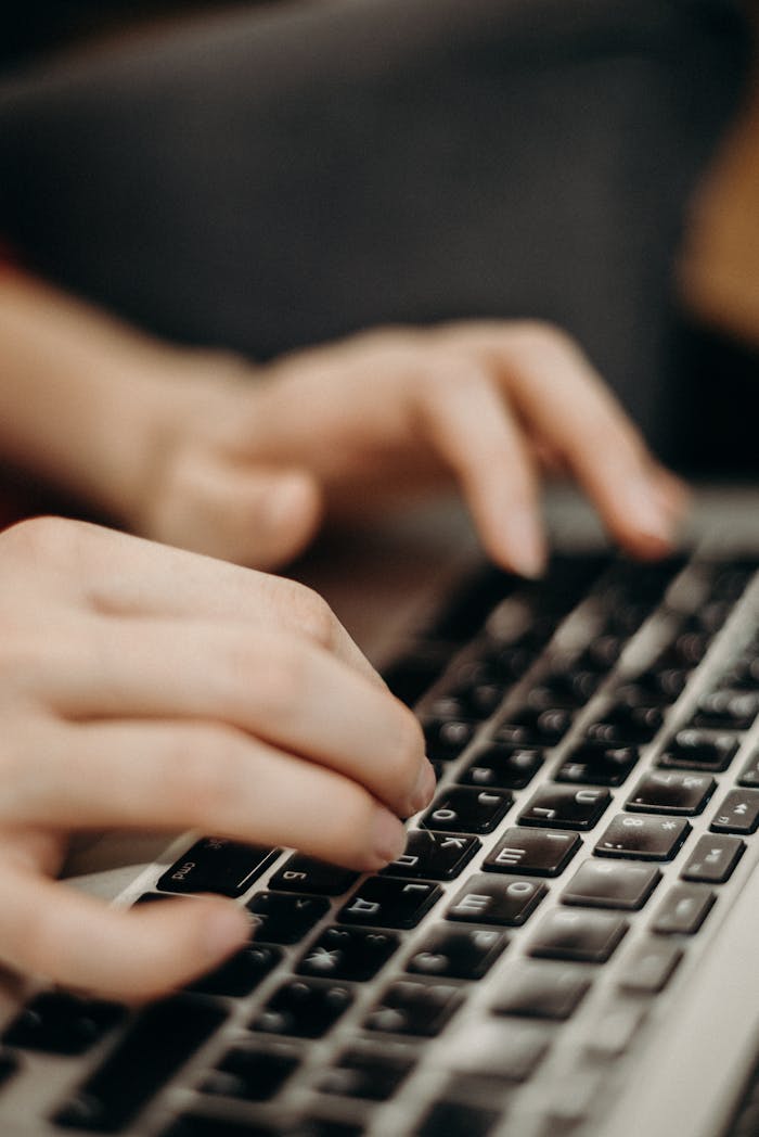 Close-up shot of hands typing on a laptop keyboard in a work environment.
